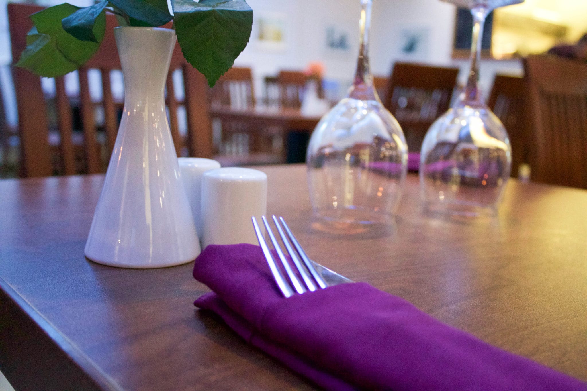 table with purple napkin around knife and fork with upside down wine glasses